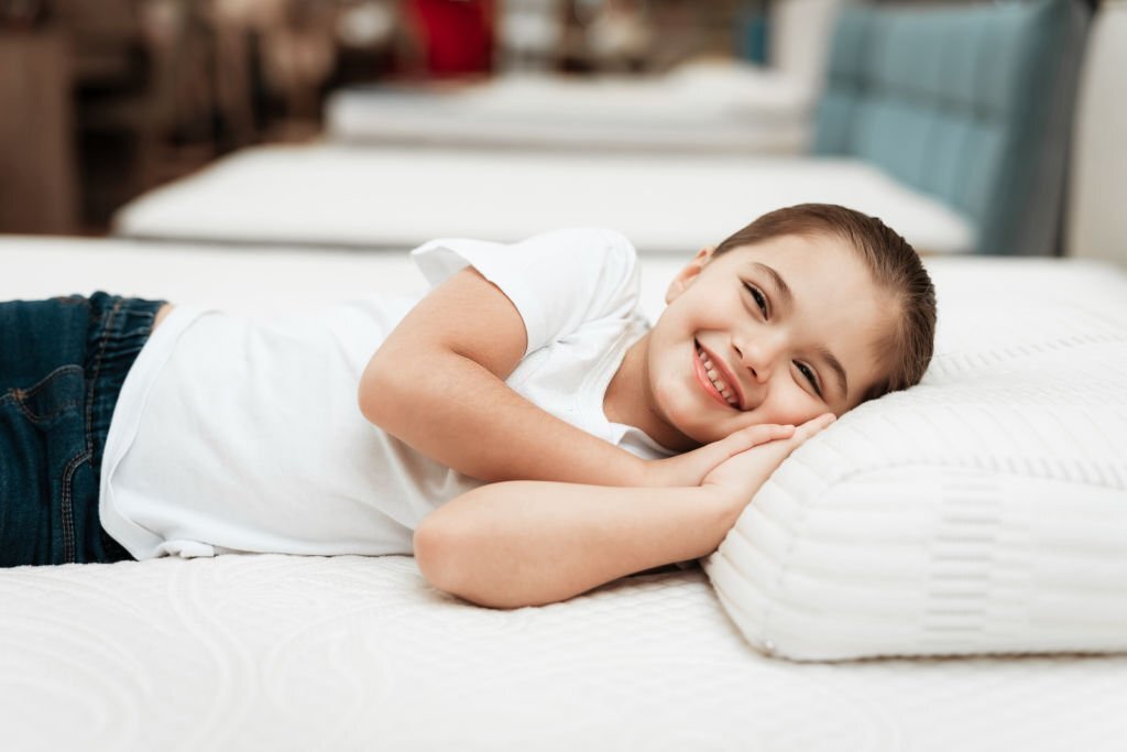Smiling little girl lies on n orthopedic mattress in a furniture store. Testing mattress. Concept of healthy posture.